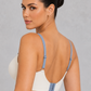 A woman shown from the back wearing a white bralette with light blue straps and matching white shorts against a textured gray studio background.