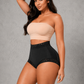 A woman modeling a two-piece shapewear set consisting of a beige strapless bandeau top and black high-waisted briefs with lace trim, set against a textured gray studio background.