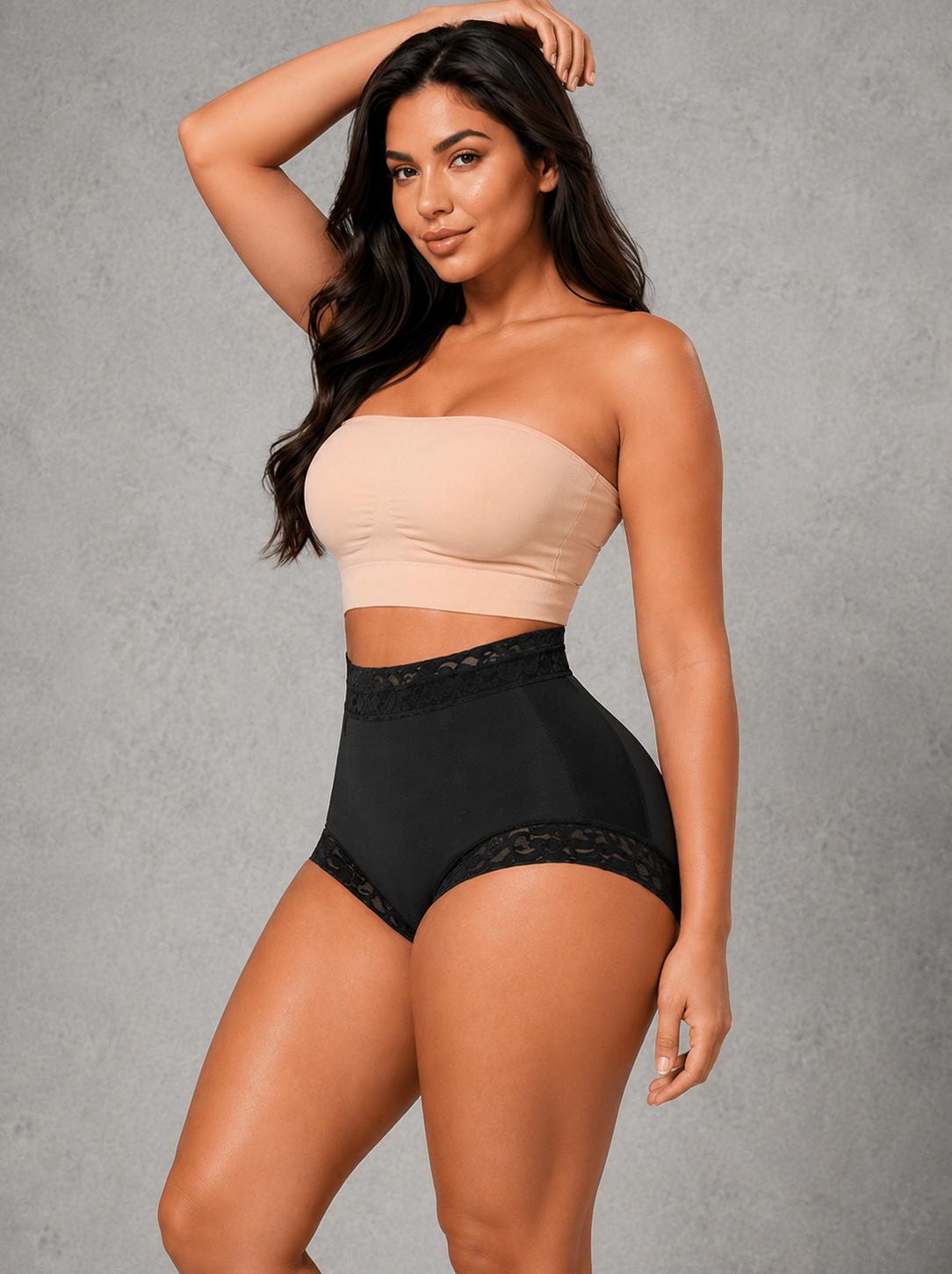 A woman modeling a two-piece shapewear set consisting of a beige strapless bandeau top and black high-waisted briefs with lace trim, set against a textured gray studio background.