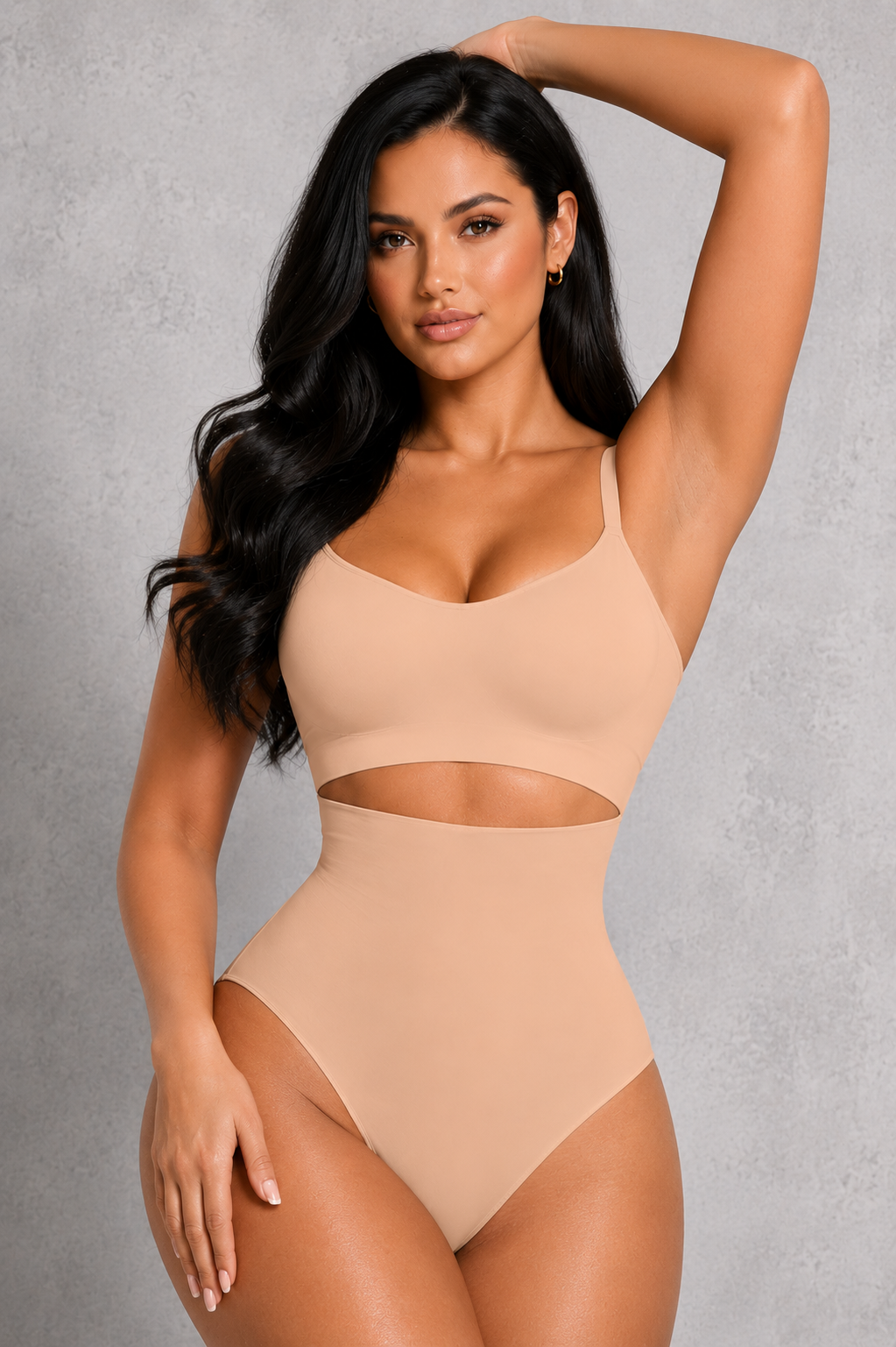 A woman modeling a beige two-piece shapewear set consisting of a bralette and high-waisted briefs with a midriff cutout, set against a textured gray studio background.