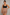 A plus-size woman modeling a black scoop-neck crop top and high-waisted shapewear shorts in a nude shade, standing against a textured gray studio background.