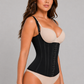 A woman modeling a black structured waist trainer corset over a beige bra and matching beige underwear, photographed against a plain light gray studio background.