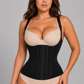 A woman modeling a black structured waist trainer corset over a beige bra and matching beige underwear, photographed against a plain light gray studio background.