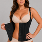 A woman modeling a black waist trainer corset over a beige bra and matching underwear, holding one side of the black waist support panel open against a plain gray studio background.