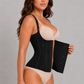 A woman modeling a black waist trainer corset over beige underwear, holding a matching black panel against a plain light gray studio background.