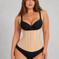 A plus-size model wearing a beige structured waist trainer corset with black underwired bra and black briefs, standing against a textured light gray studio background.