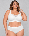 A woman wearing a light beige wireless bralette with a sheer mesh V-neckline detail, paired with light-wash blue jeans.