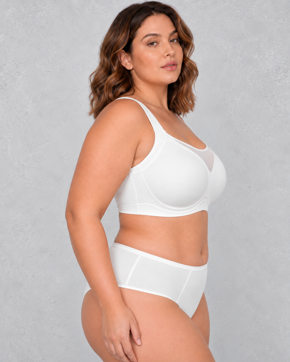A woman wearing a light beige wireless bralette with a sheer mesh V-neckline detail, paired with light-wash blue jeans.