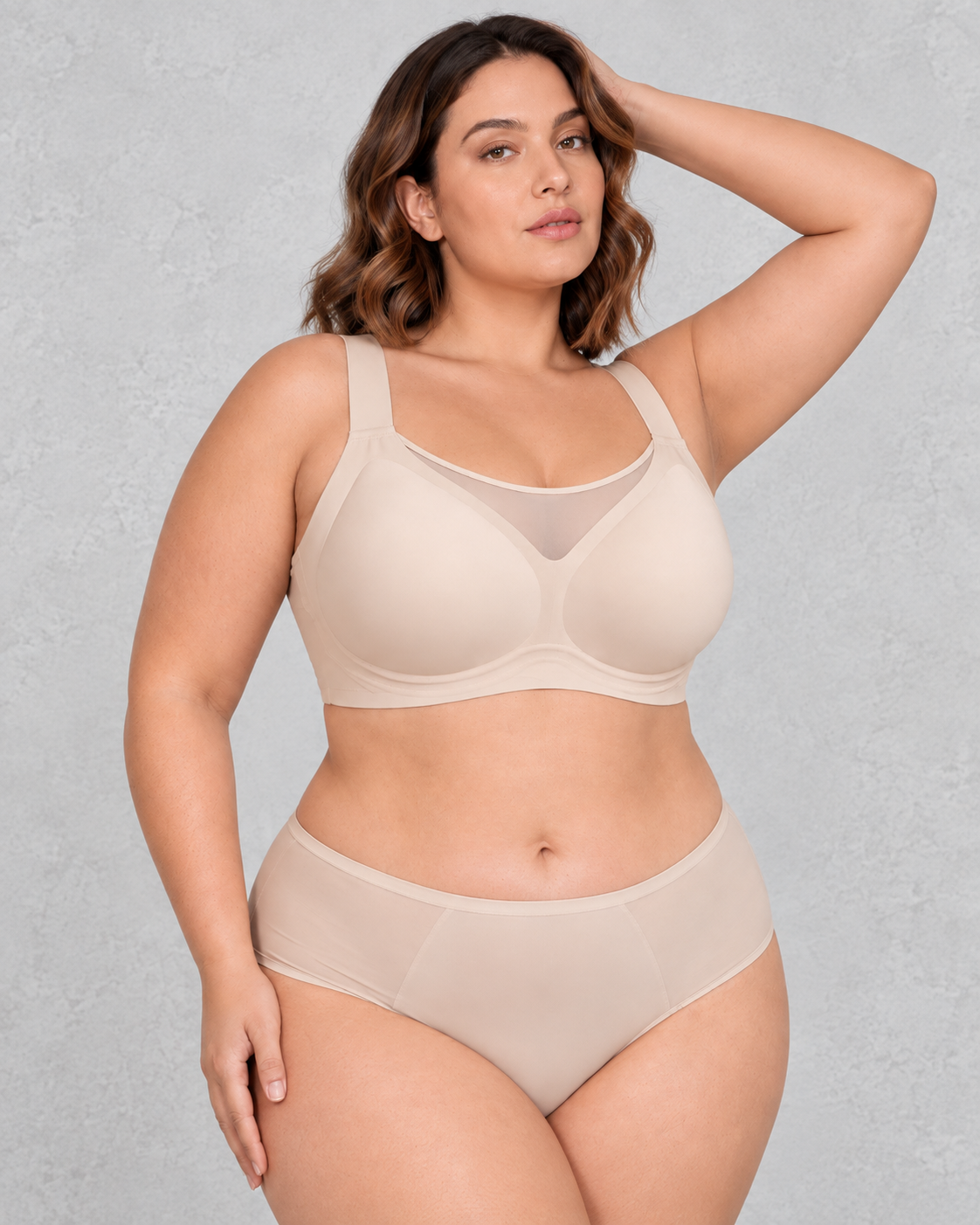 A woman wearing a light beige wireless bralette with a sheer mesh V-neckline detail, paired with light-wash blue jeans.
