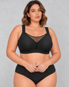 A woman wearing a light beige wireless bralette with a sheer mesh V-neckline detail, paired with light-wash blue jeans.