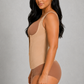 A woman modeling a beige bodysuit and matching high-waisted briefs against a plain gray studio background.