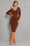 A woman modeling a long-sleeve, bodycon midi dress in a rich brown color, standing against a textured gray studio wall.