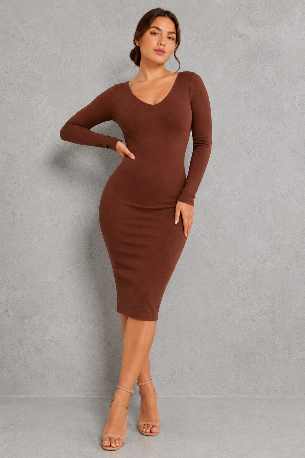 A woman modeling a long-sleeve, bodycon midi dress in a rich brown color, standing against a textured gray studio wall.
