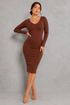 A woman modeling a long-sleeve, bodycon midi dress in a rich brown color, standing against a textured gray studio wall.
