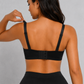 A woman shown from the back wearing a black bralette with adjustable shoulder straps and a hook-and-eye back closure, paired with black bottoms, against a light gray textured background.