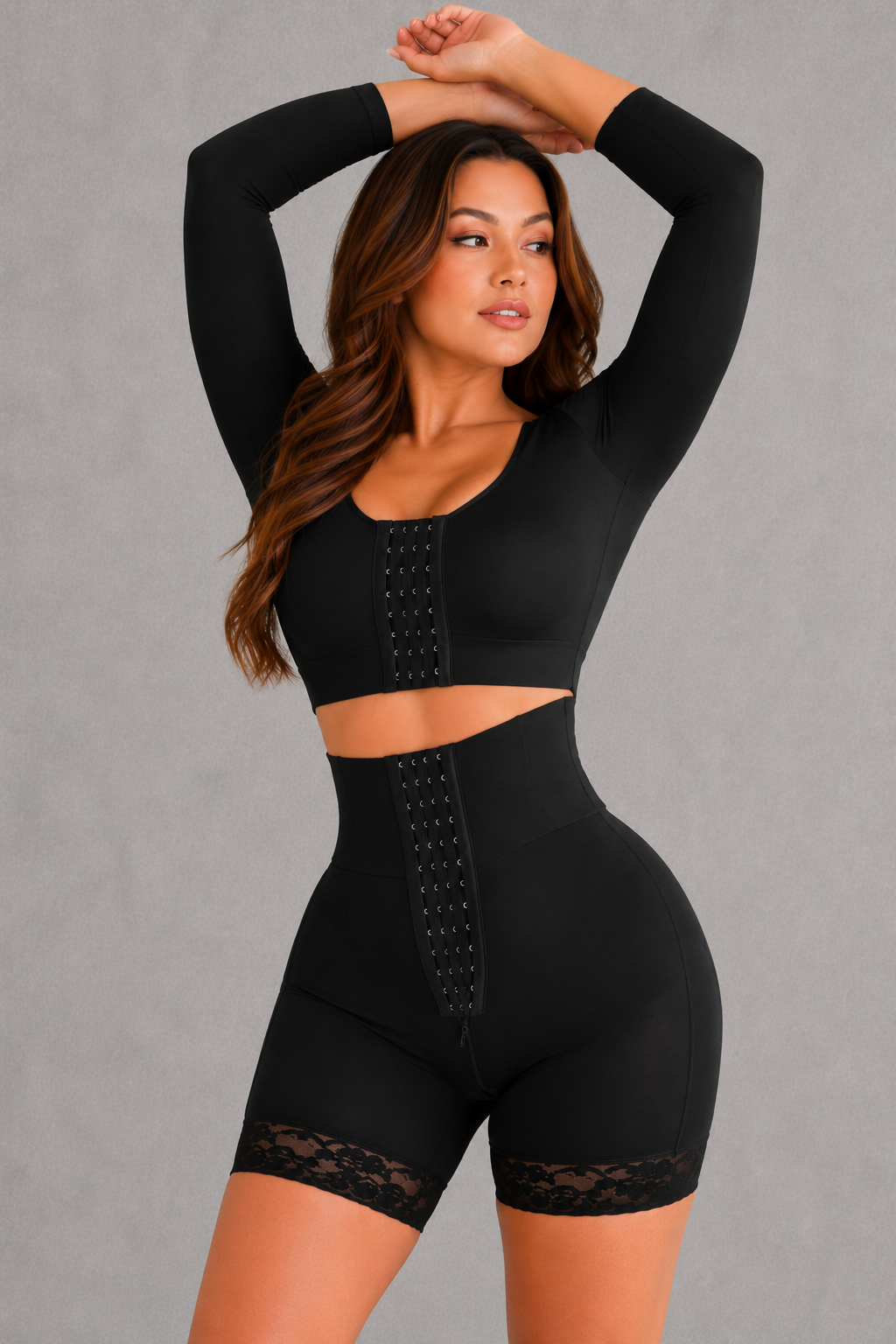 A woman modeling a black two-piece activewear set consisting of a long-sleeve crop top and high-waisted shorts with lace trim and lace-up front details, set against a plain gray studio background.
