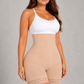 A woman modeling a beige high-waisted shapewear bodysuit with a white camisole top, standing against a textured gray studio background.