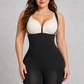 A woman modeling a black shapewear bodysuit with a built-in cream bra, standing against a textured gray studio background.