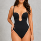 A woman modeling a black one-piece bodysuit with a keyhole cutout at the bust, thin shoulder straps, and high-cut legs, posed against a textured gray studio background.