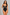 A woman modeling a black one-piece bodysuit with a keyhole cutout at the bust, thin shoulder straps, and high-cut legs, posed against a textured gray studio background.