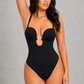 A woman modeling a black one-piece swimsuit with a keyhole cutout at the bust, photographed against a plain light gray studio background.